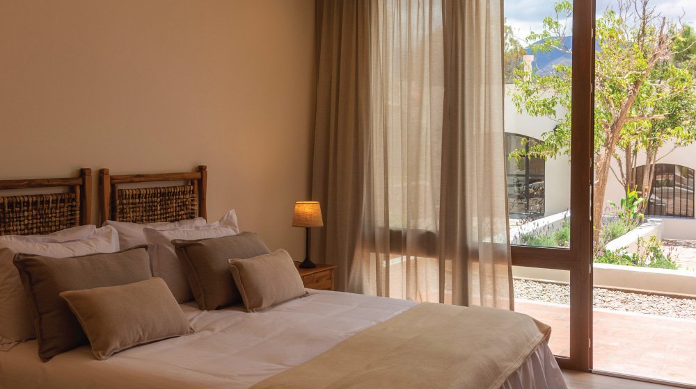 Cama doble y vista a los cerros de las habitaciones estándar en planta baja con aire acondicionado del Hotel El Candil en Tilcara, Jujuy.